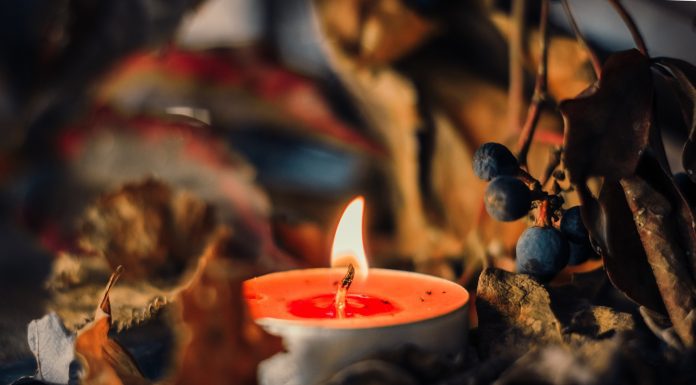 A lit orange tea light candle surrounded by fall leavess and