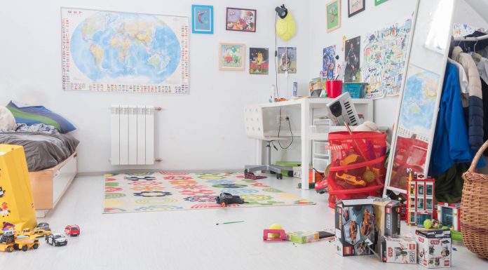 children's room with posters and map on the wall, toys cluttered on the floor and dresser, and a messy bed