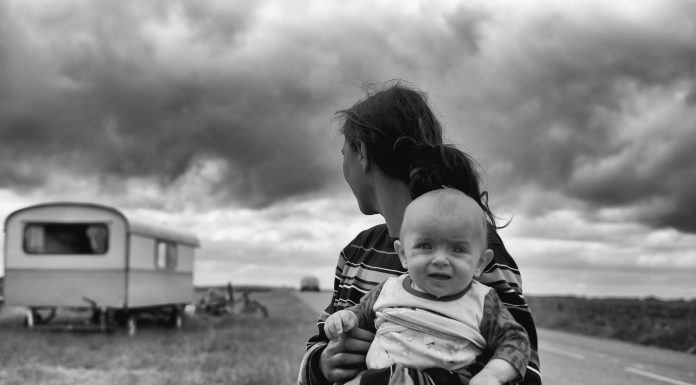 parent holding a child in a dry land with a trailer in the background, black and white photo