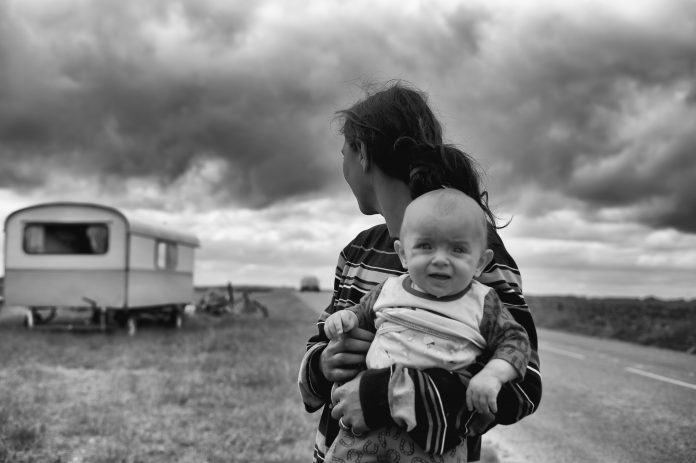 parent holding a child in a dry land with a trailer in the background, black and white photo