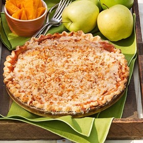 crunch top apple pie on a green cloth with apples and carrots in the background