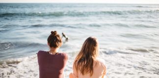 two women sitting on the beach and staring out at the ocean