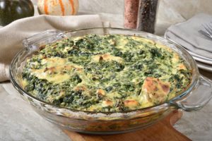 spinach casserole in a clear dish on a wood table