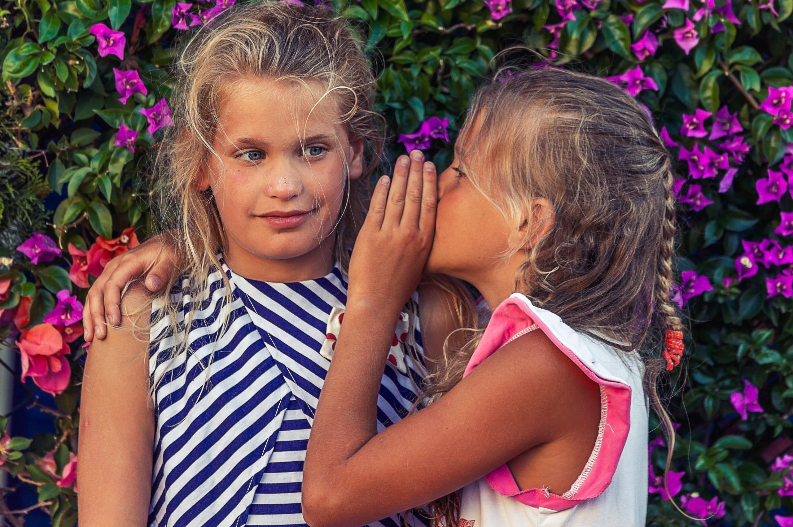 two young tweens whispering to one another in purple flowers