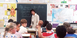 a classroom of kids with a teacher in front of a blackboard