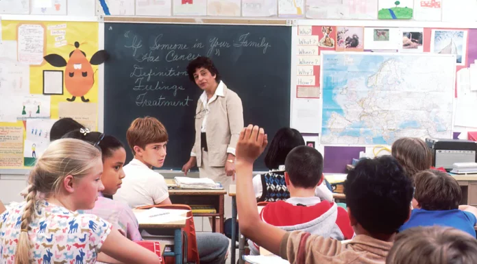 a classroom of kids with a teacher in front of a blackboard