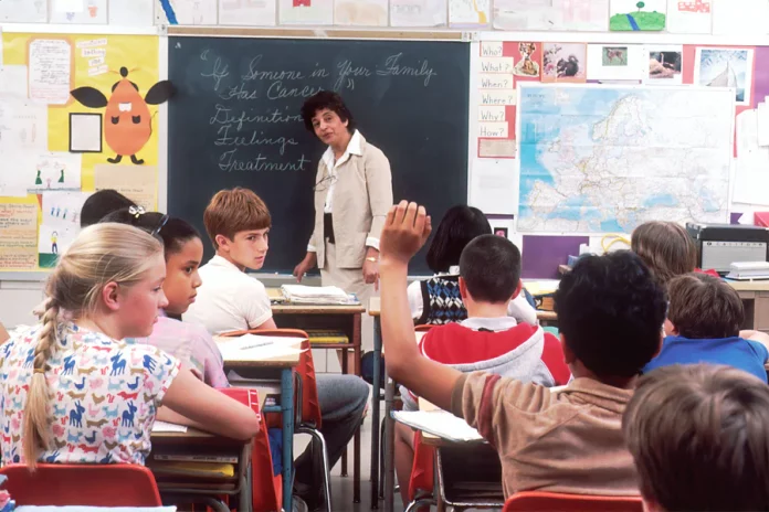 a classroom of kids with a teacher in front of a blackboard