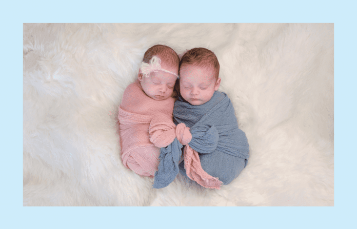 twin babies in pink and blue wraps on a white fluffy blanket