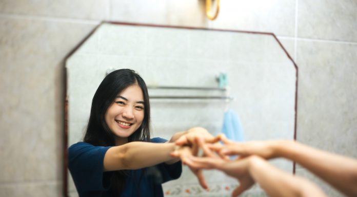 Young adult Asian woman practices positive self-talk in the mirror