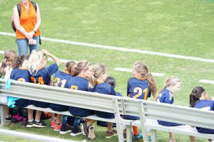 a team of kids, sitting on a bench on a field 