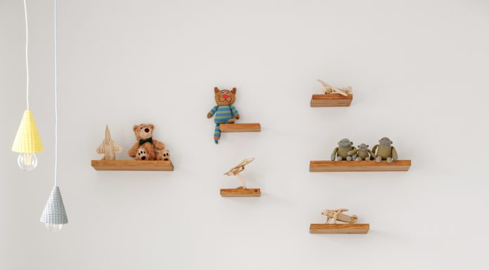 Natural wood Montessori-style toddler bed with pillows, small blanket. Toys sit on shelves mounted high above the bed.