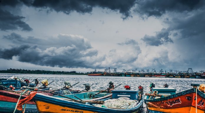 Wooden boats can be seen in the foreground with storm clouds in the sky behind them.