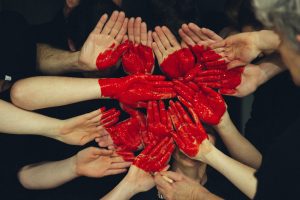 several hands are shown, face up, with a red heart painted across them.