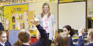 teacher standing in a classroom with students raising their hands