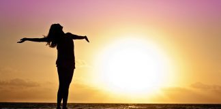 A woman stands on a deck during a sunset and stares at the beach.