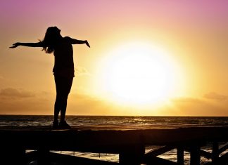 A woman stands on a deck during a sunset and stares at the beach.