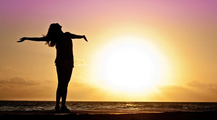 A woman stands on a deck during a sunset and stares at the beach.