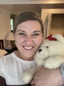 A woman smiles while holding a dingy, well loved white bear.