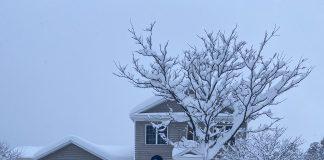 Man using snow blower to clear walk way in several feet of snow.