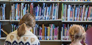 Two children read books in front of library shelves.