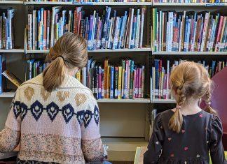 Two children read books in front of library shelves.