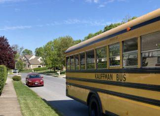 A yellow school bus is the main focus. It is pulling away on a residential street