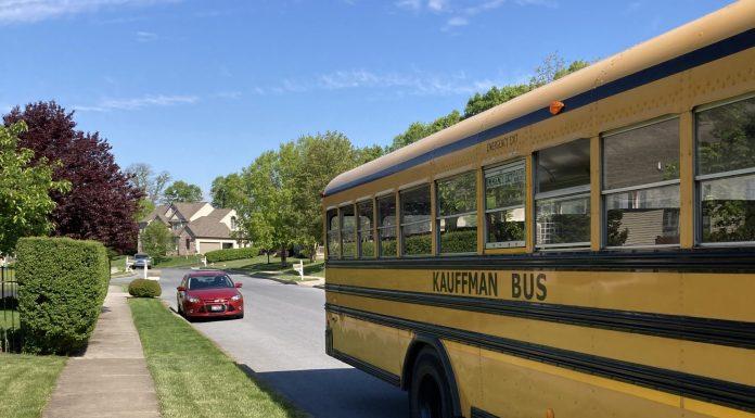 A yellow school bus is the main focus. It is pulling away on a residential street