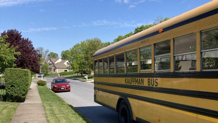 A yellow school bus is the main focus. It is pulling away on a residential street