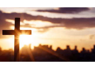 Sun setting behind a cross with a city on the horizon