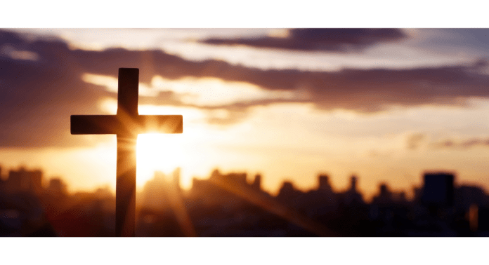 Sun setting behind a cross with a city on the horizon