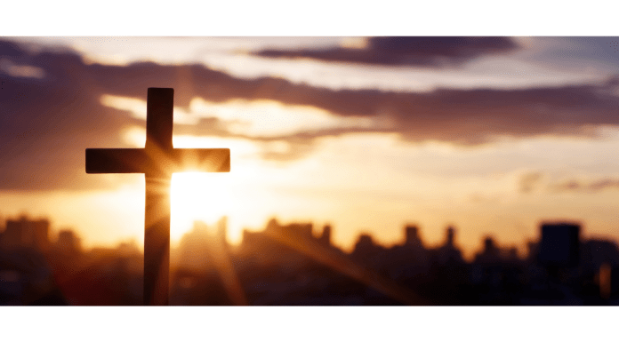 Sun setting behind a cross with a city on the horizon