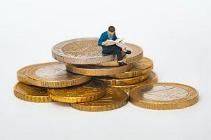 A small figure sits on top of a stack of coins.