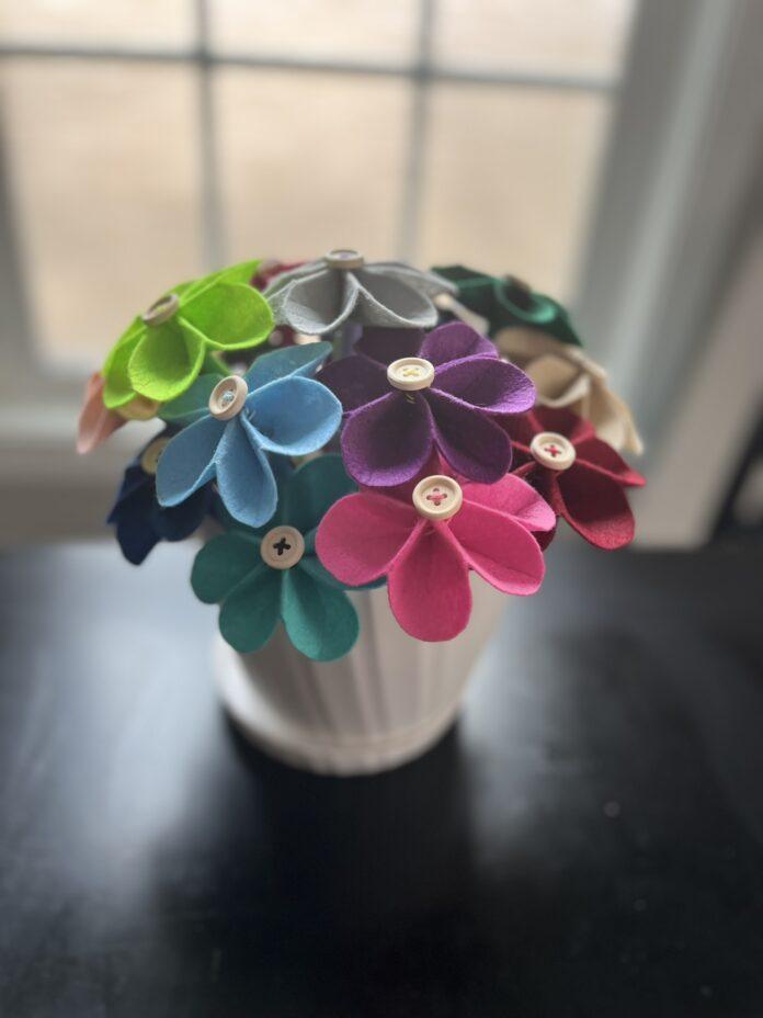 Multicolored bouquet of felt flowers with wooden button centers in a white flower pot