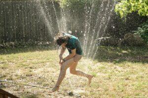 girl running through the sprinkler for water sensory play