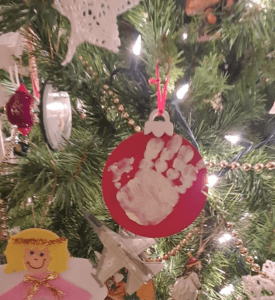 Red painted ornament with white handprint hanging on a Christmas tree