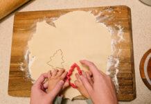 hands of mother and child cutting out tree shaped sugar cookie together