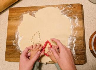 hands of mother and child cutting out tree shaped sugar cookie together