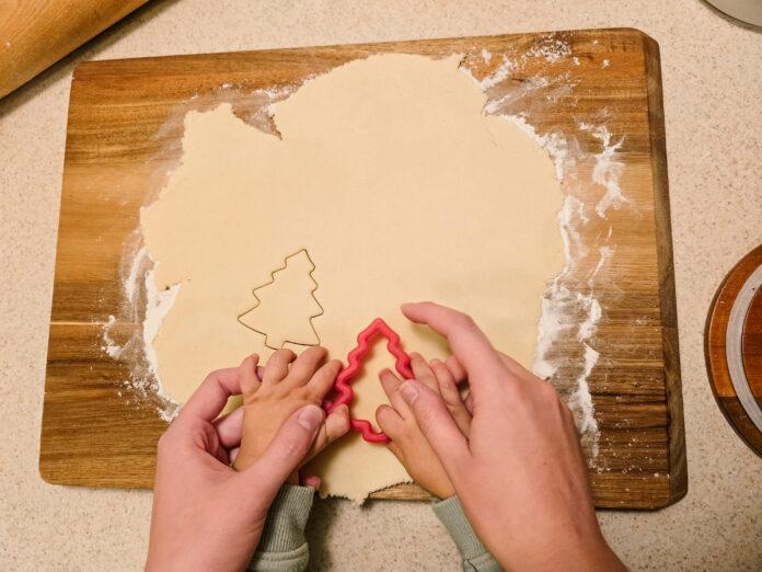 hands of mother and child cutting out tree shaped sugar cookie together