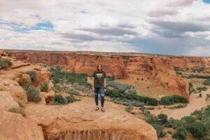 Woman standing on cliff with rock formations in the background in Canyon de Chelly National Monument in Northern Arizona