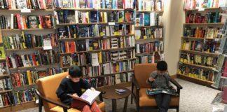 Improving Your Kids’ Literacy Begins at Home Picture of two young boys sitting and reading books in a library, using the easy tips to improve literacy.