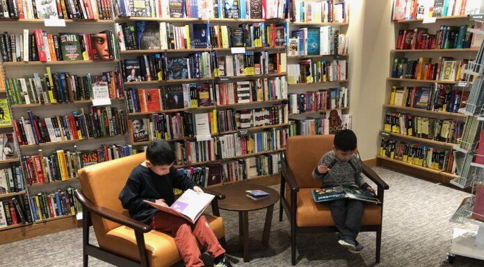 Improving Your Kids’ Literacy Begins at Home Picture of two young boys sitting and reading books in a library, using the easy tips to improve literacy.