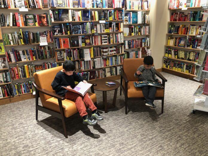library Picture of two young boys sitting and reading books in a library, using the easy tips to improve literacy.