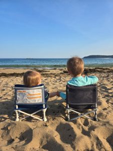 2 children sitting in beach chairs facing the ocean